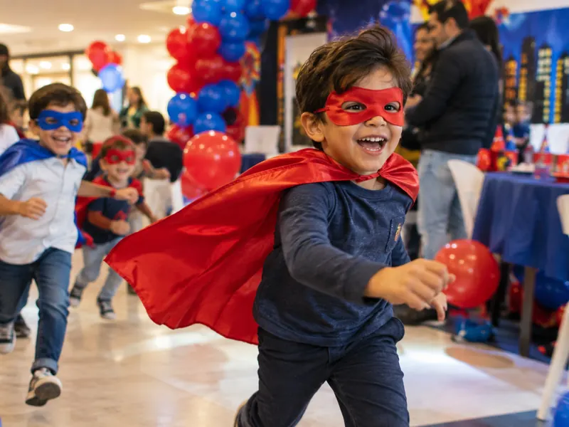 Niño con capa roja y antifaz corriendo en una fiesta temática de superhéroes en Bogotá